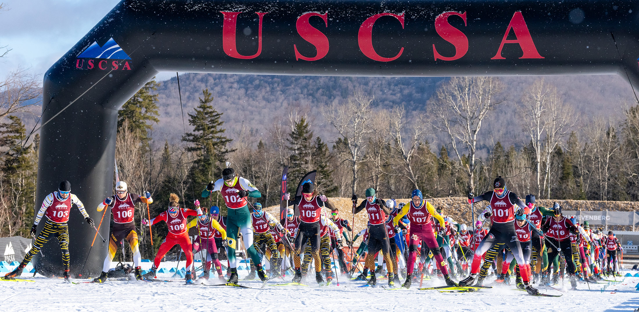 Men’s 15 km freestyle mass start explodes off the line under the USCSA arch at Mt. Van Hoevenberg, with a deep collegiate field charging into the race.