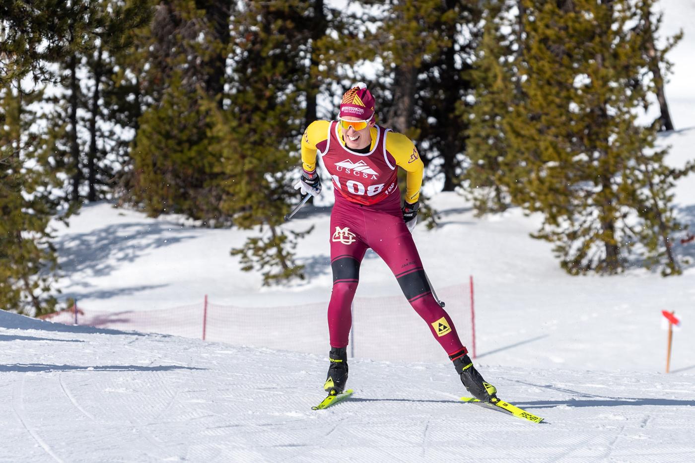 Cross country skier in CMU uniform racing on groomed snow with trees in the background.