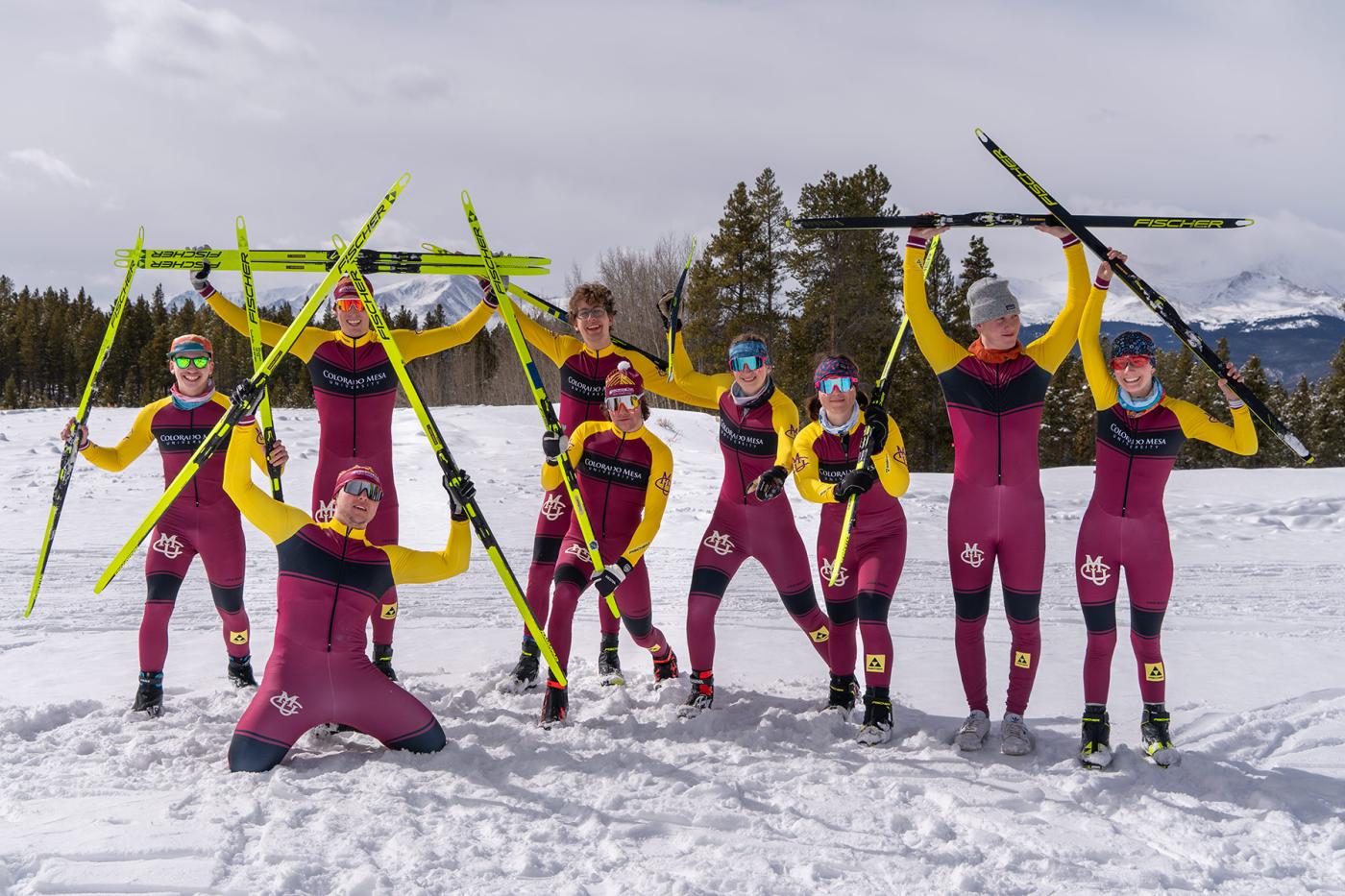 Colorado Mesa University cross country ski team posing in maroon and yellow uniforms, holding skis in the snow.